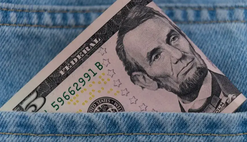 A five dollar bill tucked into a blue denim jeans pocket, symbolizing savings or cash on the go.
