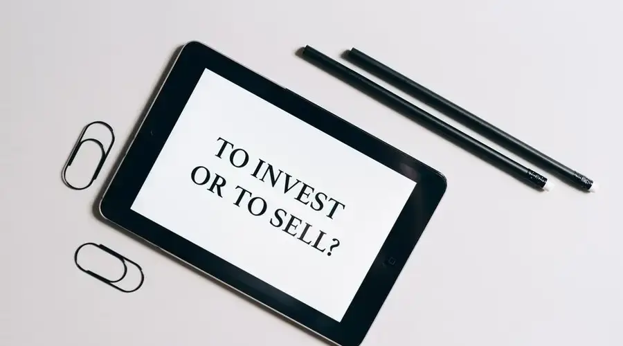 Flat lay of tablet with investment decision text, surrounded by stationery on a white table.