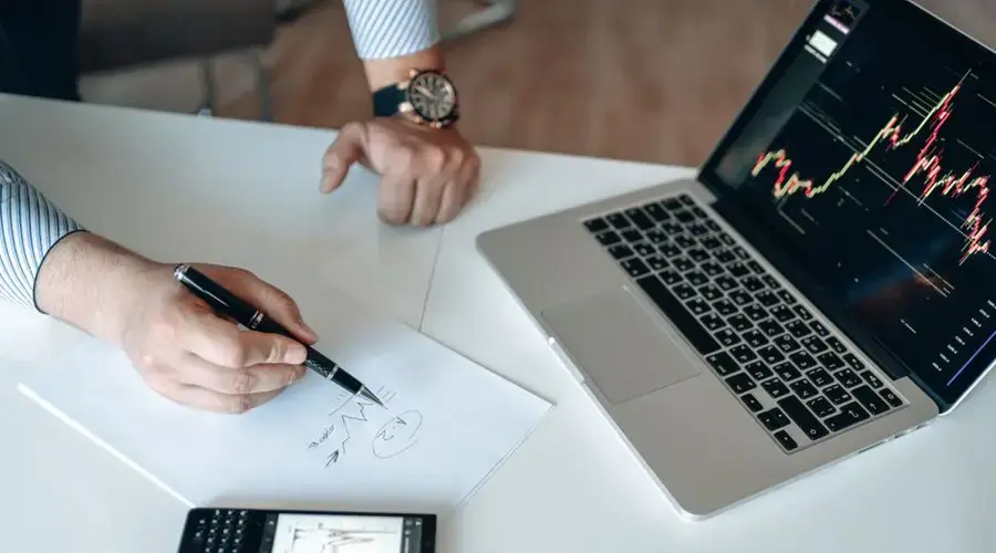 Hands analyzing financial data at a workspace with a laptop and paper graphs, perfect for business settings.
