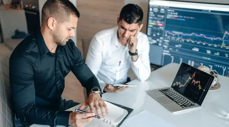 Two professionals discussing market trends with digital devices and charts in an office setting.