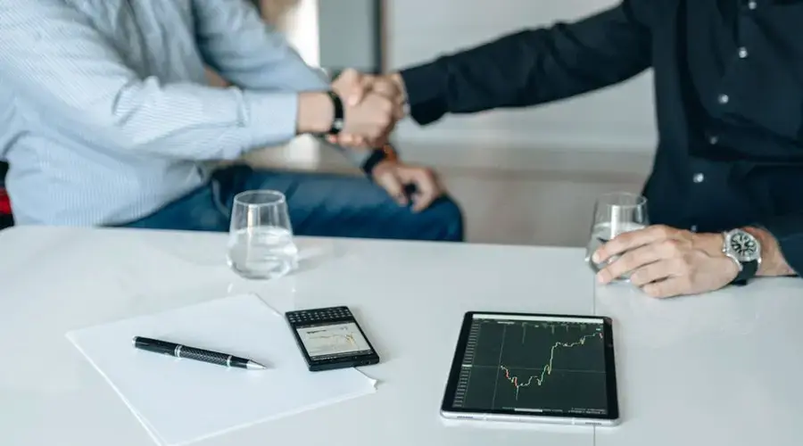 Business meeting with handshake and financial analysis displayed on a tablet.