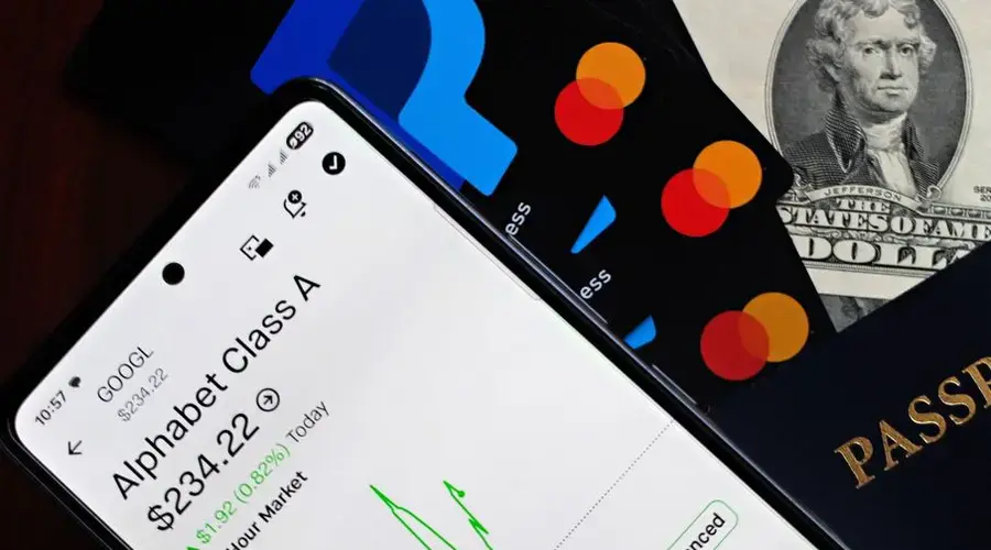 A smartphone displaying Alphabet stock price alongside credit cards, cash, and passport.