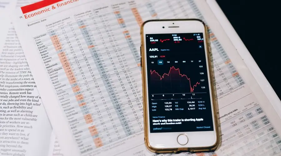 Smartphone displaying stock market data on papers with financial charts.