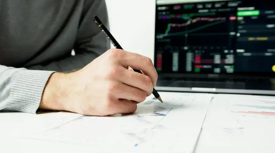 Close-up of a person analyzing financial charts with a laptop displaying stock market data.