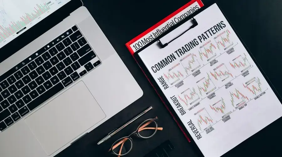 Flat lay of a workspace with trading patterns, charts, and a laptop on a black background, ideal for finance themes.