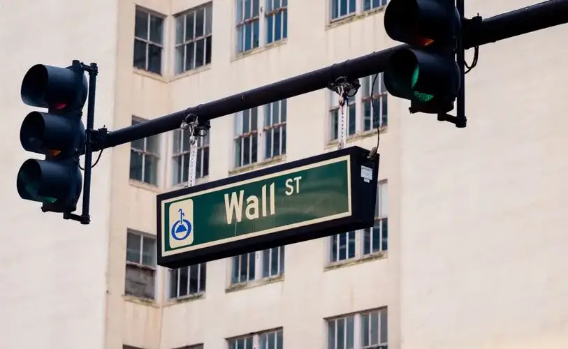 Traffic lights and Wall St sign in cityscape, symbolizing finance hub.