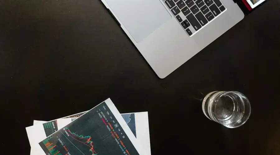 Professional workspace featuring financial graphs, laptop, and glass of water on a sleek desk.