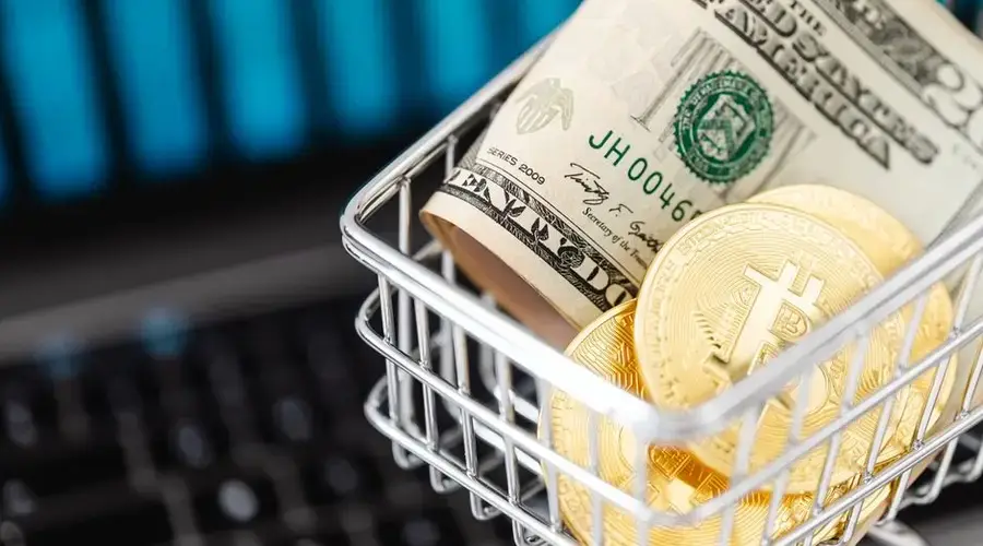 Close-up of bitcoin coins and US dollars in a shopping cart on a laptop, symbolizing digital finance.
