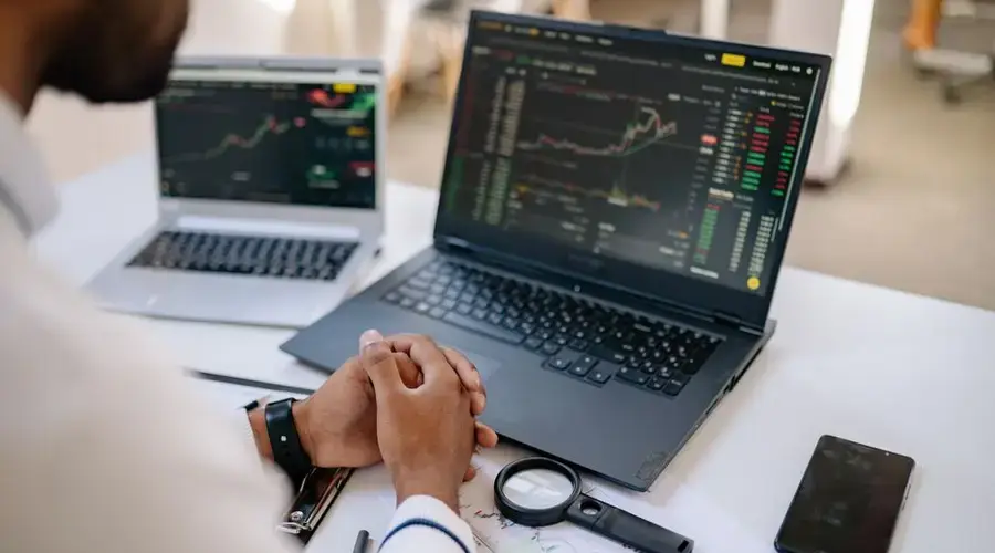 Business professional analyzing stock market data on dual laptops in an office.