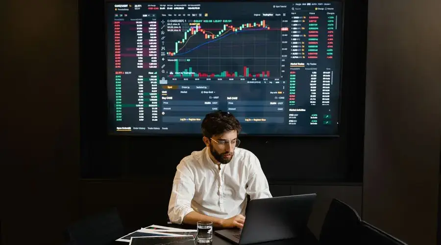 Focused businessman analyzing stock market data on laptop with financial graphs displayed on screen.