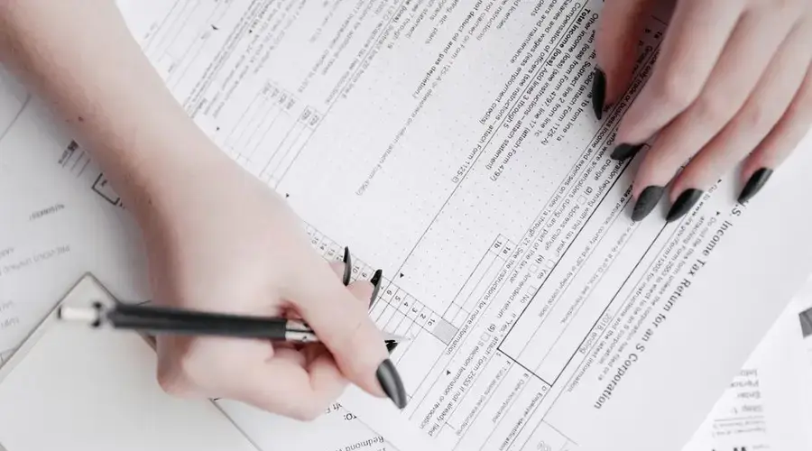 A detailed close-up of a woman filling out tax forms with a pen. Ideal for finance themes.