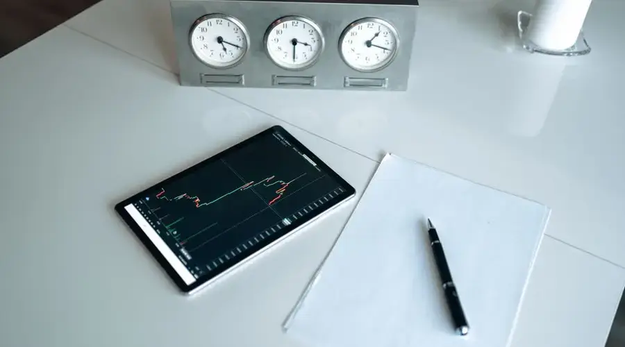 Tablet showing stock chart next to clocks and pen on desk. Perfect for business and finance themes.