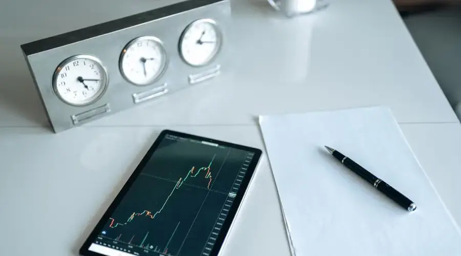 Tablet displaying stock chart on a minimal white workspace with clock and pen.