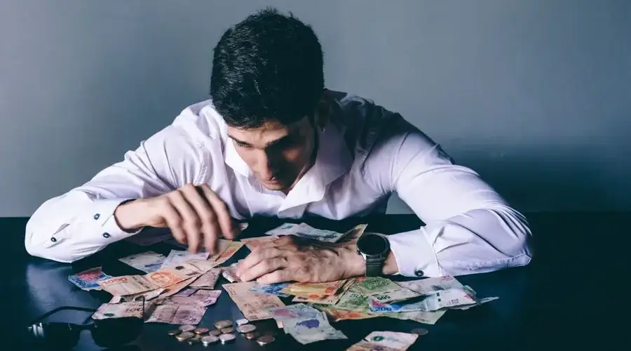 Focused man counts various international currencies on a dark desk indoors.