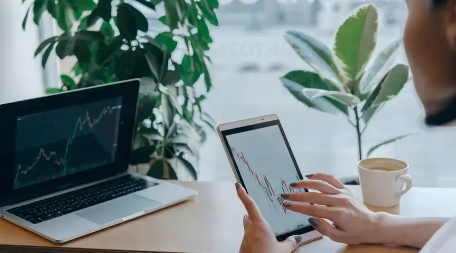 A professional analyzes stock market graphs on a tablet, symbolizing modern finance and remote work.