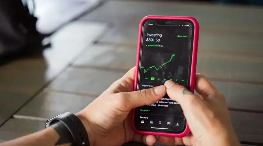 A person holding a smartphone with a stock market app displaying analytics and stock prices.