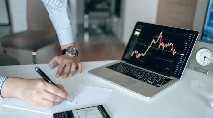Professional workspace with a laptop displaying financial graphs and a person writing.