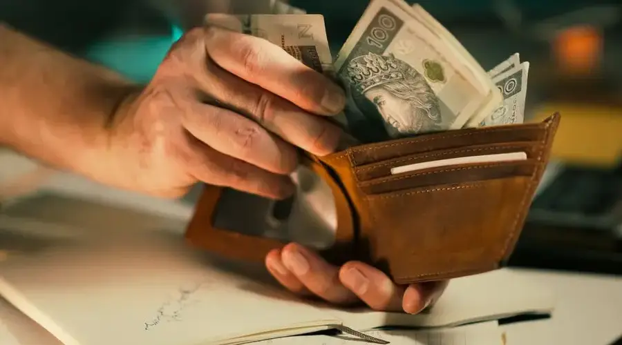 A close-up of hands holding a wallet filled with Polish banknotes on a desk.