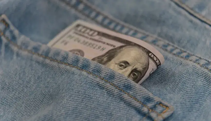 Close-up of a 100 dollar bill in a denim pocket, symbolizing finance and savings.