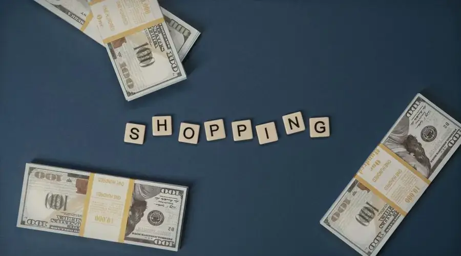 Stacked US dollars around shopping letters on a blue background.