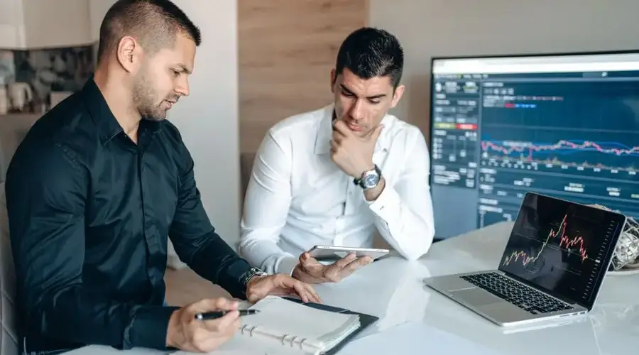 Two businessmen discussing stock market analytics in a modern office setting.