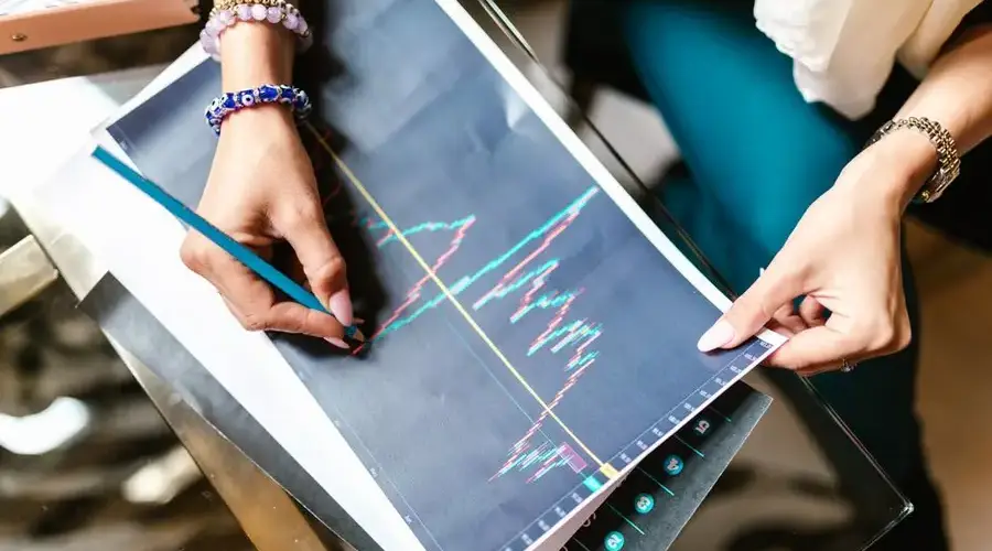 Woman analyzing financial graph with a printout on a glass table holding a pencil.