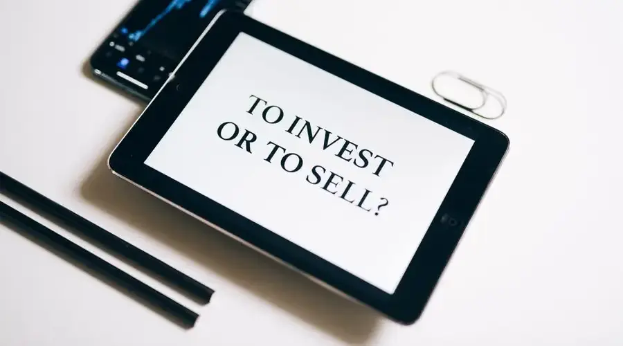 A tablet with text 'To Invest or To Sell?' on a white background.