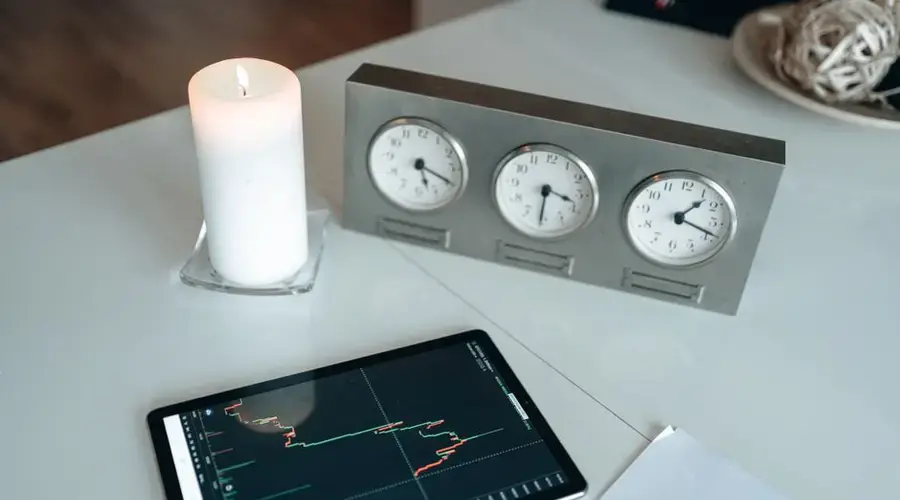 Tablet displaying trading charts on a sleek desk with clocks and a candle.