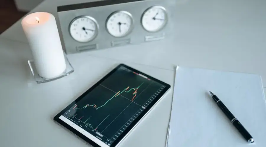 Tablet showing trading graph beside candle and papers in an office setting.