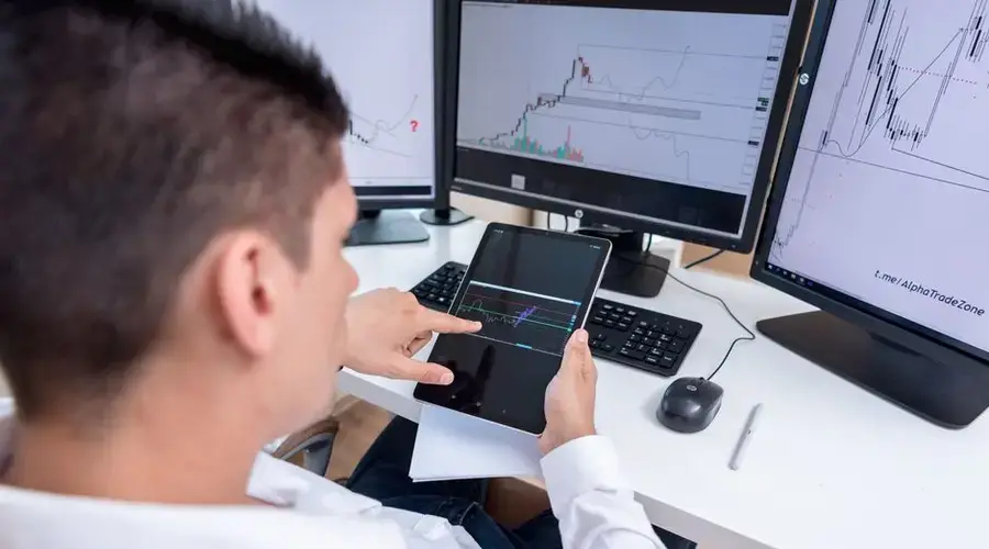 A stock trader analyzing cryptocurrency charts on multiple monitors and a tablet.