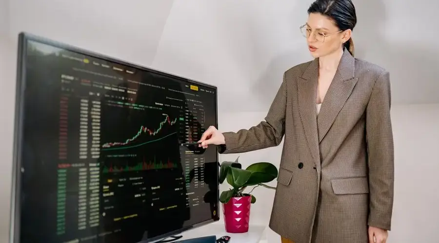 Businesswoman using stylus to highlight stock data on a monitor in office.