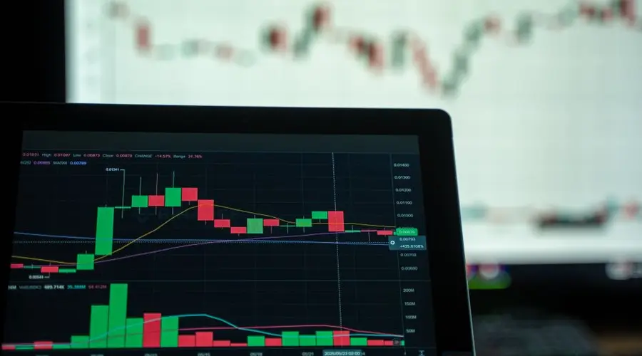 A laptop displays a detailed cryptocurrency trading chart with candlestick patterns.