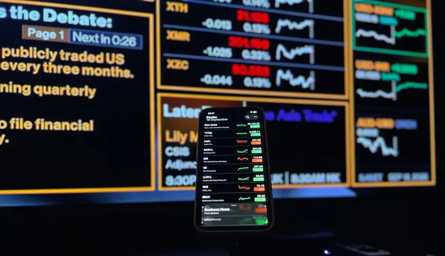 Smartphone displaying stock market data against financial screen backdrop in London.