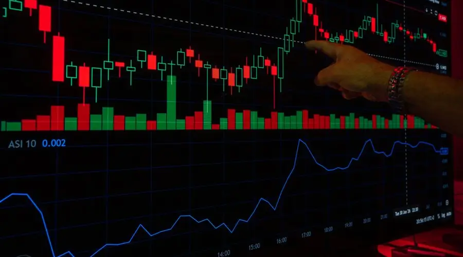 A hand points at a stock market graph on a digital screen, highlighting financial trading trends.