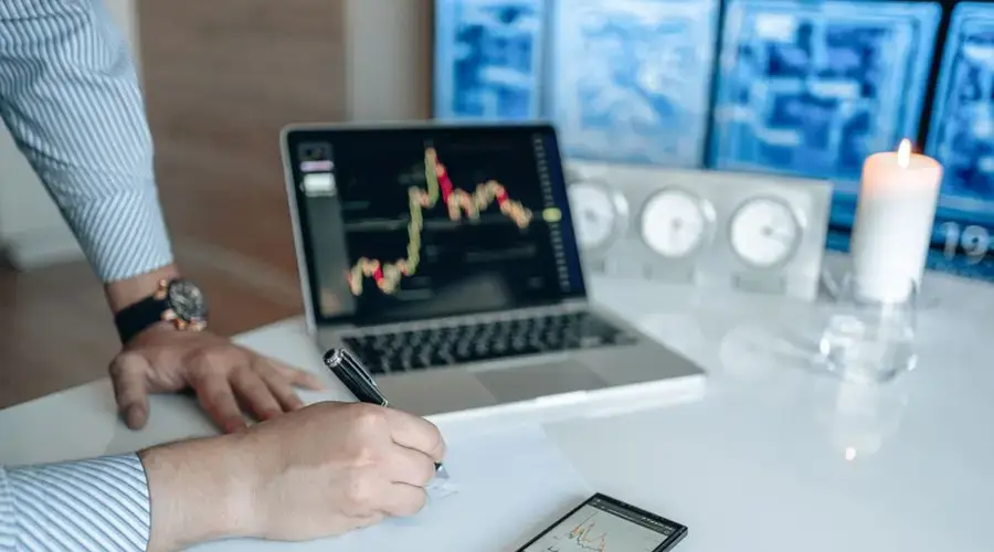 Man analyzing stock market trends on a laptop, writing notes on paper.