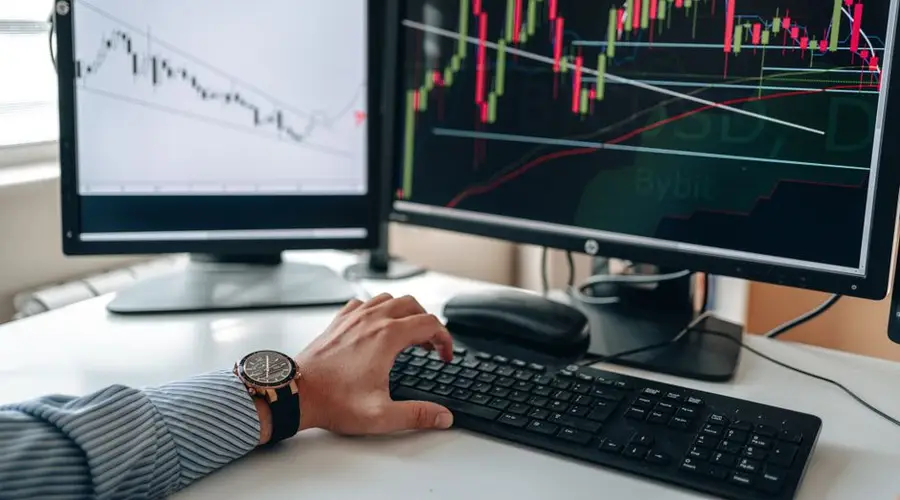 A businessperson using dual monitors to analyze stock market trends with charts and graphs.