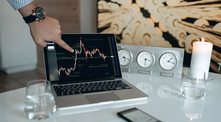 A businessman points to a stock chart on a laptop screen, indicating market analysis insights.