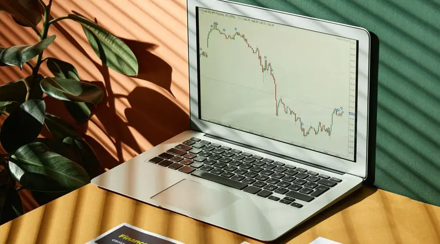 Laptop displaying a financial graph with reports, in a sunlit workspace.
