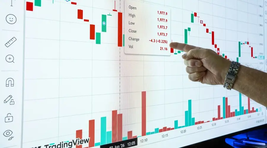 Close-up of a hand pointing at a stock market graph on a screen showing financial data.