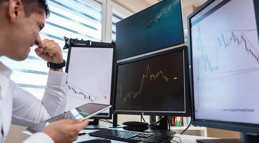 Trader in white shirt analyzing stock charts on multiple monitors during daytime in an office setting.