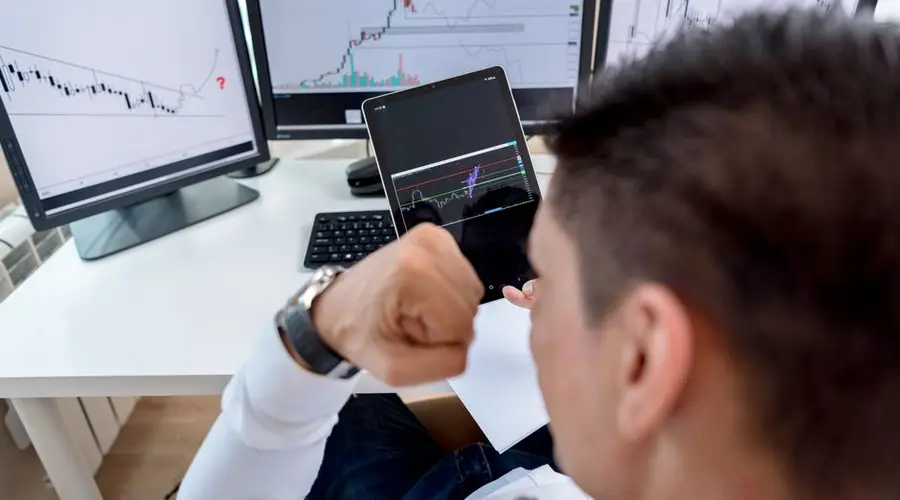 A trader confidently viewing stock market charts on multiple monitors in a modern workspace.