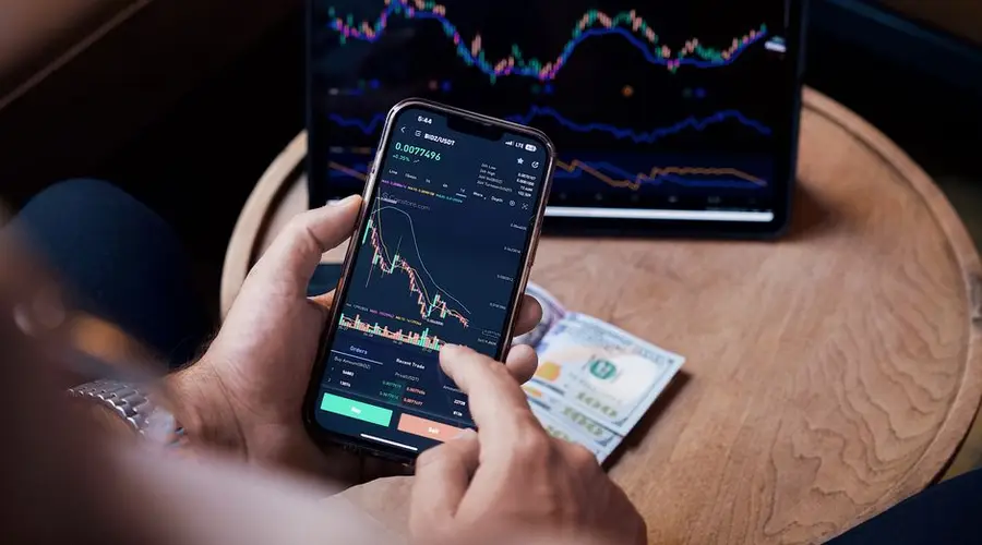 Close-up of a person trading stocks using a smartphone and a tablet.