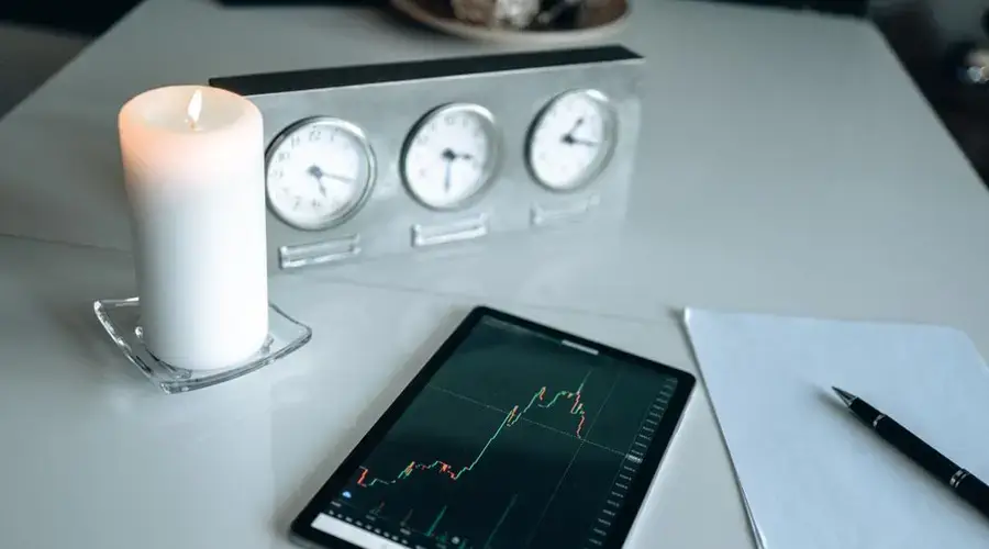 Minimalist desk setup with tablet showing trading graph alongside candle and clocks.