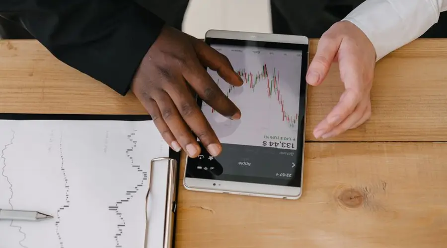 Two professionals analyzing stock market trends on a tablet in an office setting.
