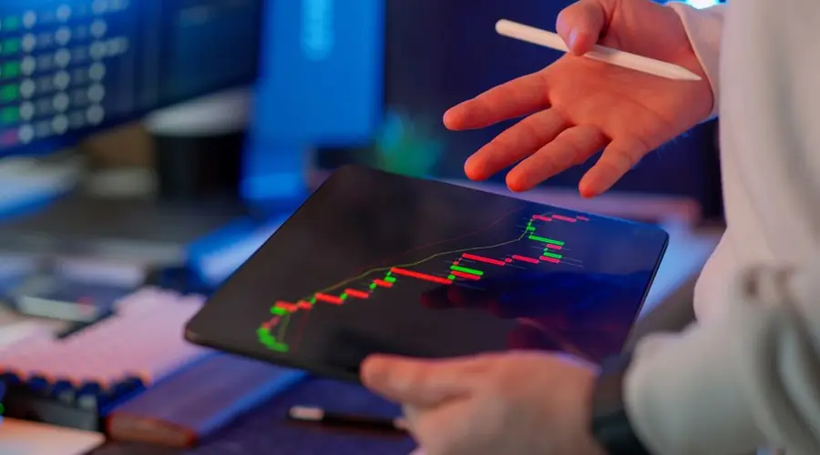 Person using a tablet to review financial and stock market data in a modern office.