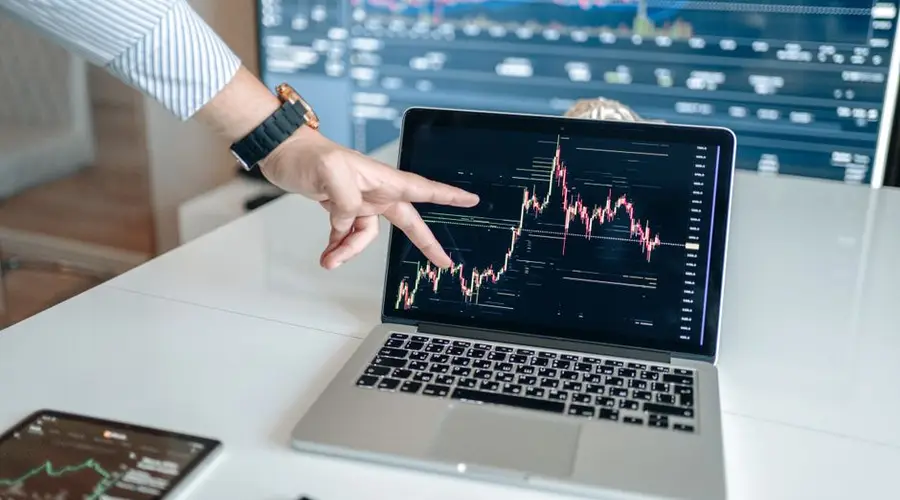 A person pointing at a laptop displaying a cryptocurrency market chart, indicating data analysis.