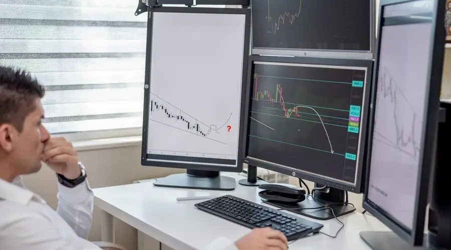 Business professional analyzing financial data on multiple computer monitors at his workspace.