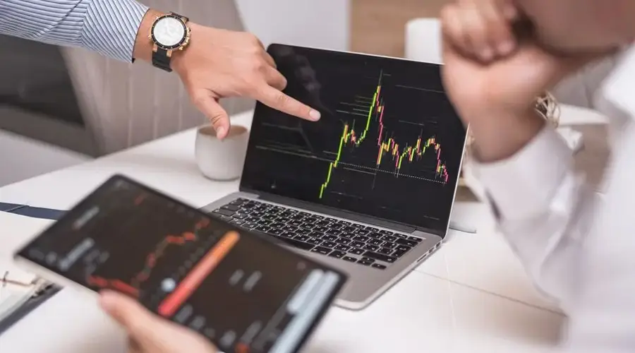 Business professionals analyzing cryptocurrency market trends on laptop and tablet.