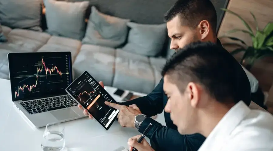 Two businessmen discussing financial charts on devices at a modern indoor setting.