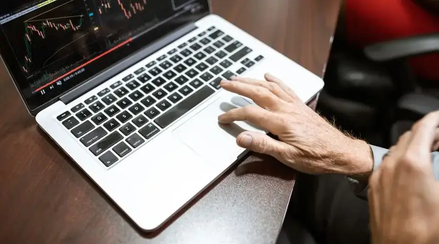 Close-up of hand using laptop for stock market analysis in office setting.